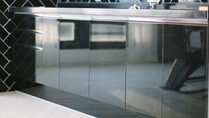 A modern kitchen with a stainless steel countertop, a built-in range hood, and a black herringbone backsplash. - Gray Hotel (Tongyeong)