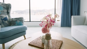 A modern living room with a round wooden coffee table, a blue armchair, and a white sofa. A vase with flowers is placed on the table. - Gray Hotel (Tongyeong)
