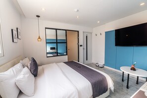 Una habitación de hotel moderna con una cama grande, televisor, una mesita y vista a la ciudad a través de un ventanal amplio.