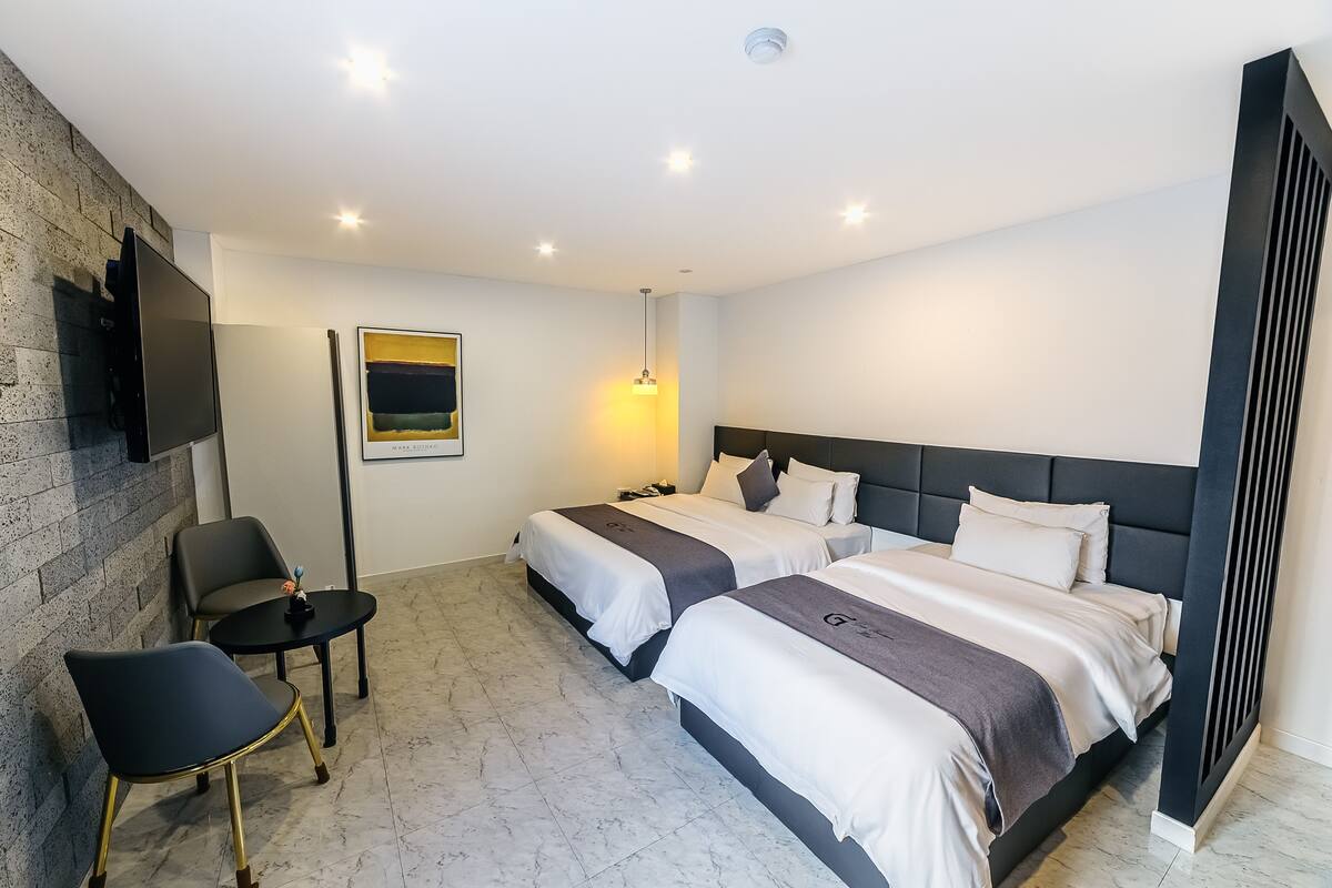 A modern hotel room with two beds, a flat-screen TV, a small table, and a chair.