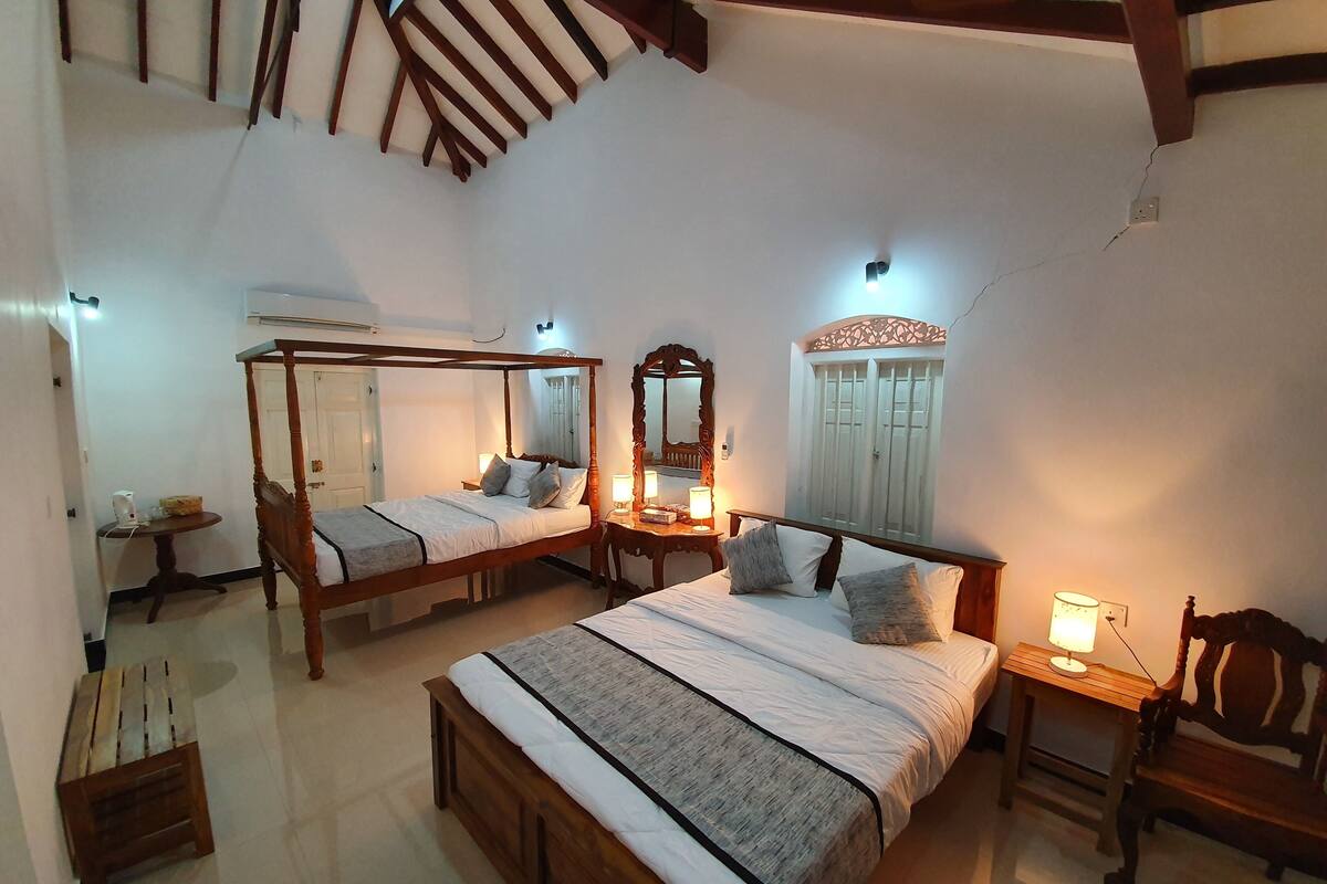 A bedroom with two wooden four-poster beds, a round wooden table, a chair, and a mirror on the wall.
