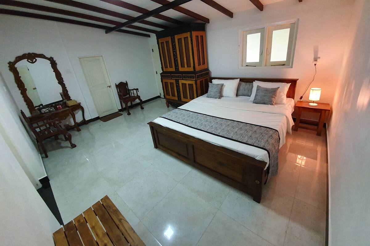 A bedroom with a wooden bed, a nightstand with a lamp, a wardrobe, a mirror, and a chair.
