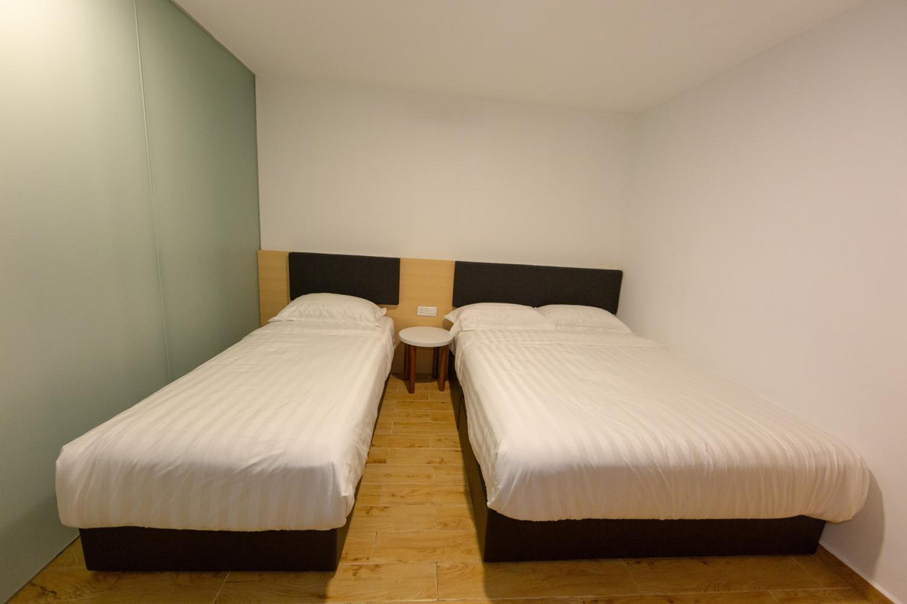 Una habitación pequeña y limpia con dos camas individuales, una mesita redonda y una pared sencilla.