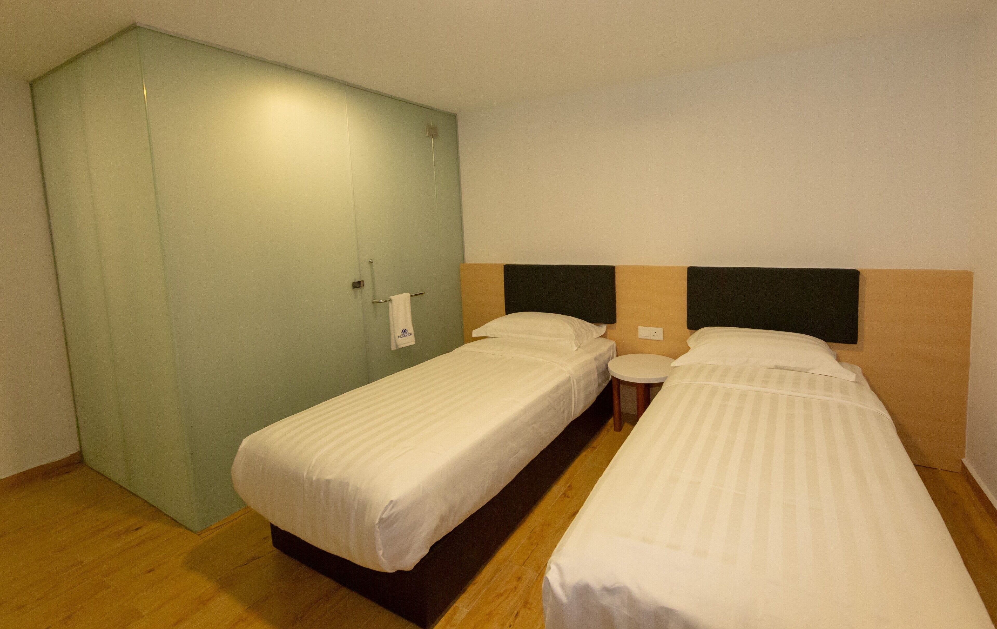 Une chambre d’hôtel avec deux lits simples, une petite table ronde et une armoire.