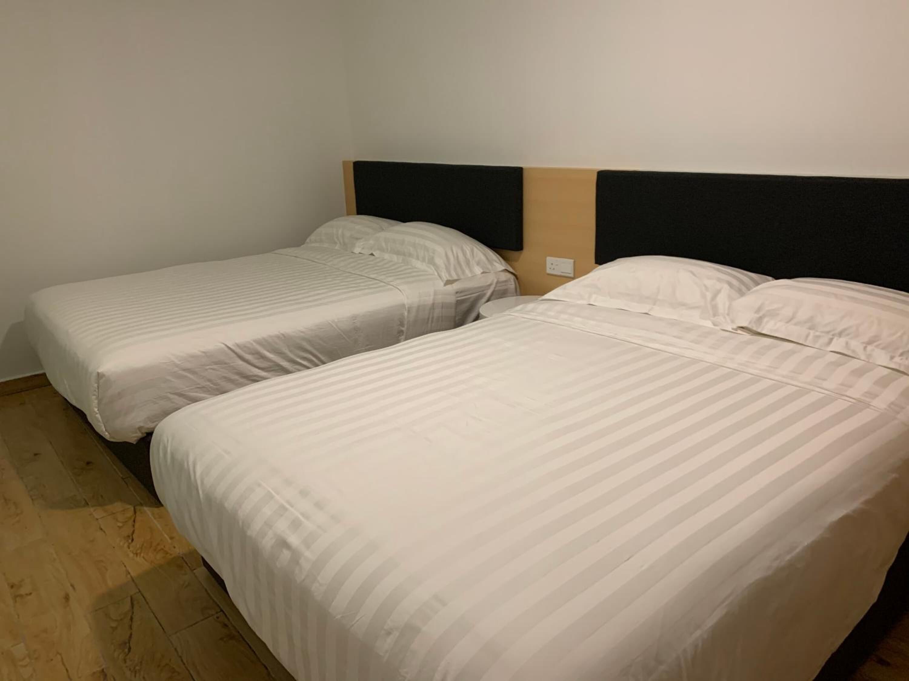 Deux lits simples avec du linge de lit blanc, dans une chambre dotée d’un plancher en bois et d’un mur uni.