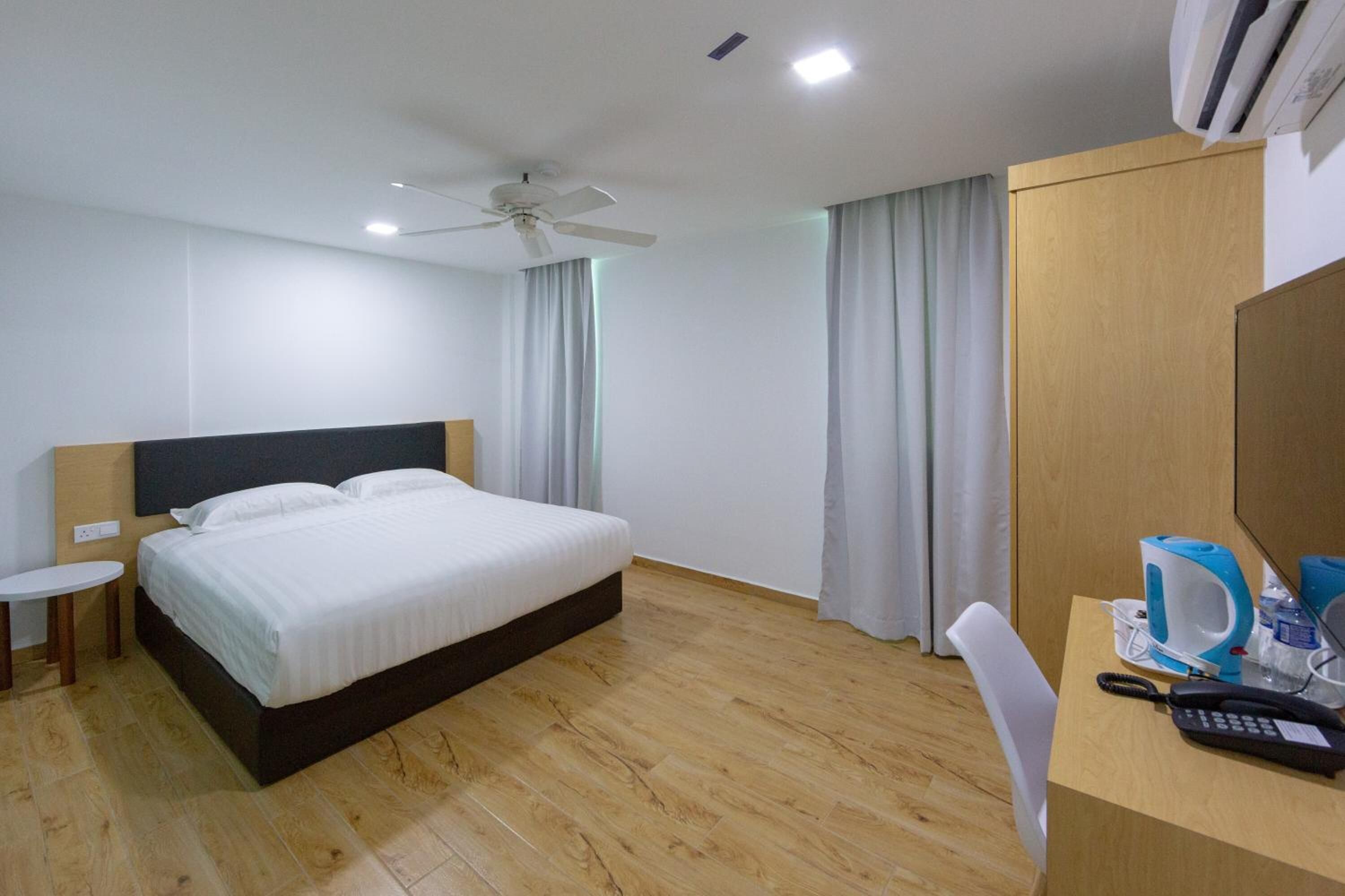A hotel room with a single bed, a desk with a telephone, a coffee maker, and a ceiling fan.