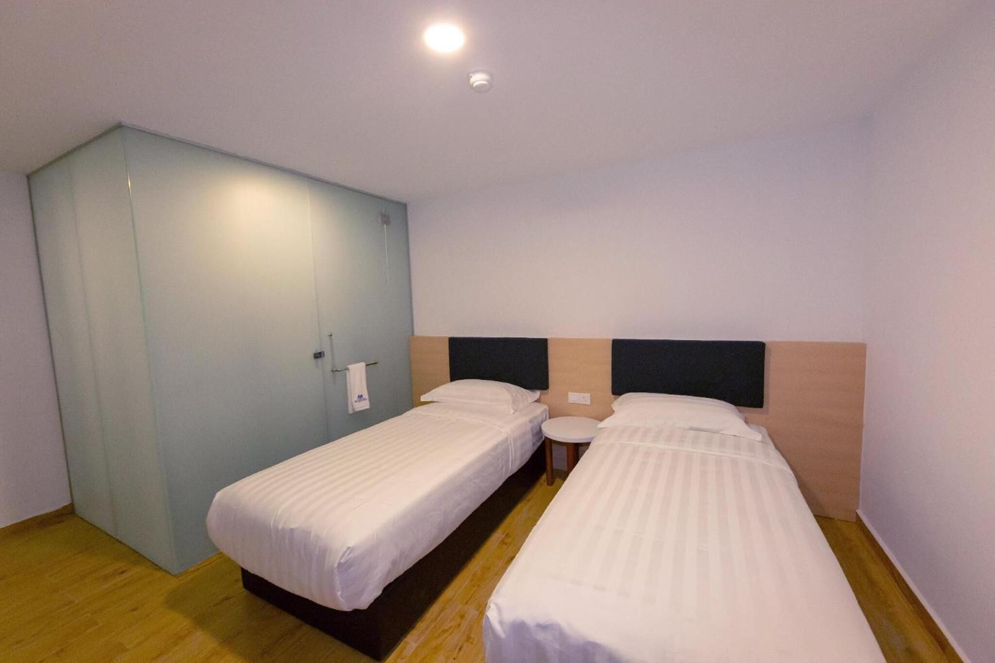 Une chambre d’hôtel avec deux lits simples, une petite table ronde et une armoire.