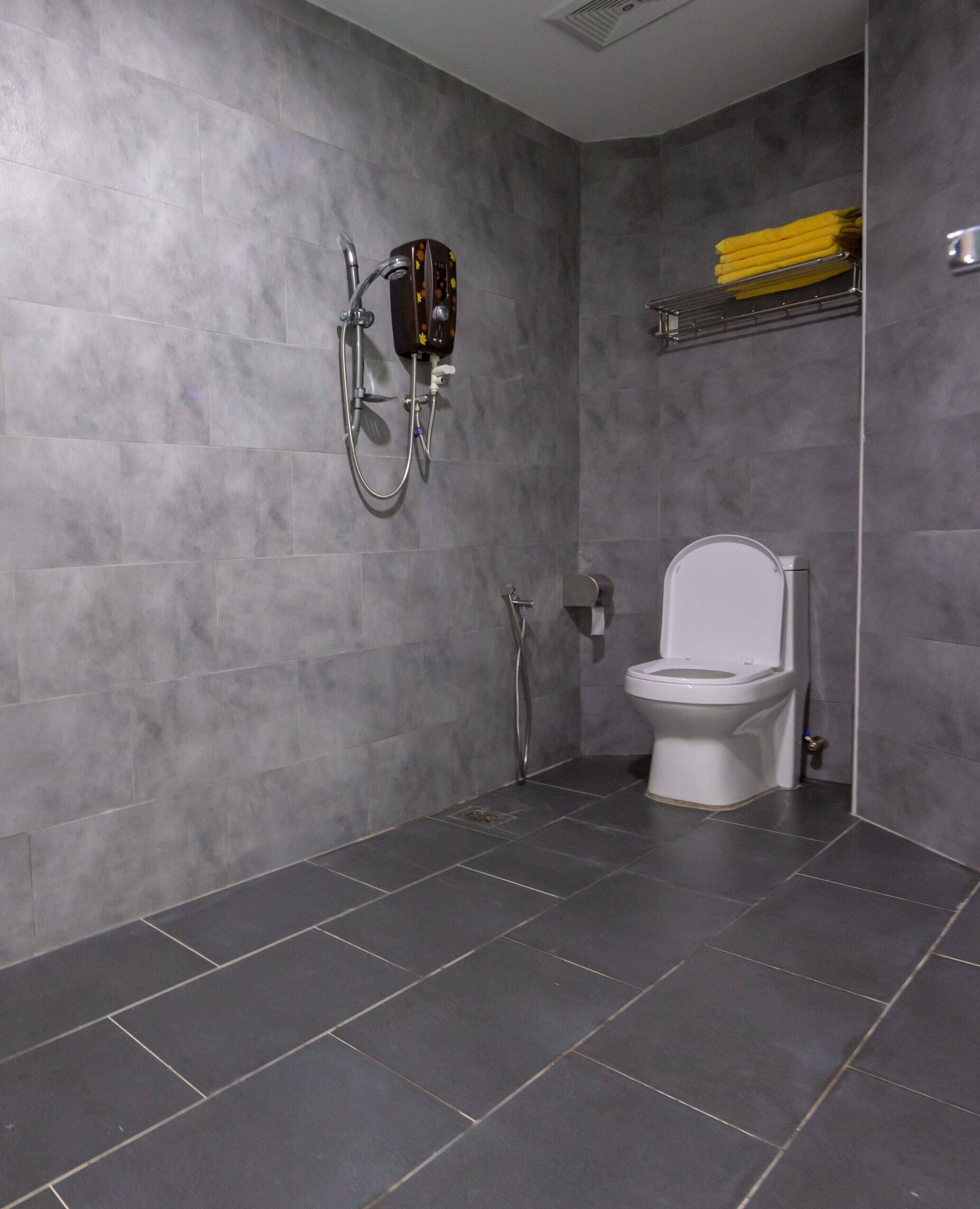 Ein modernes Badezimmer mit grauen Fliesen, einer Dusche, einer Toilette und einem Handtuchhalter.