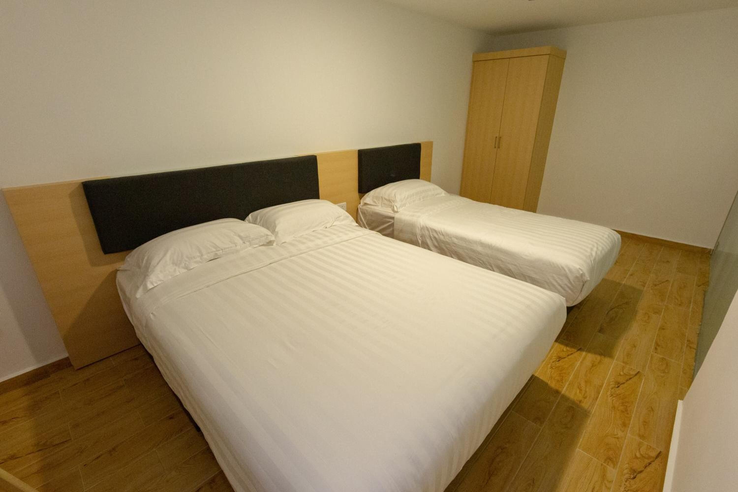 A room with two beds, a wardrobe, and wooden flooring.