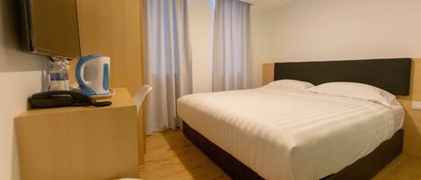 A hotel room with a bed, a desk, a chair, a television, and a coffee maker.