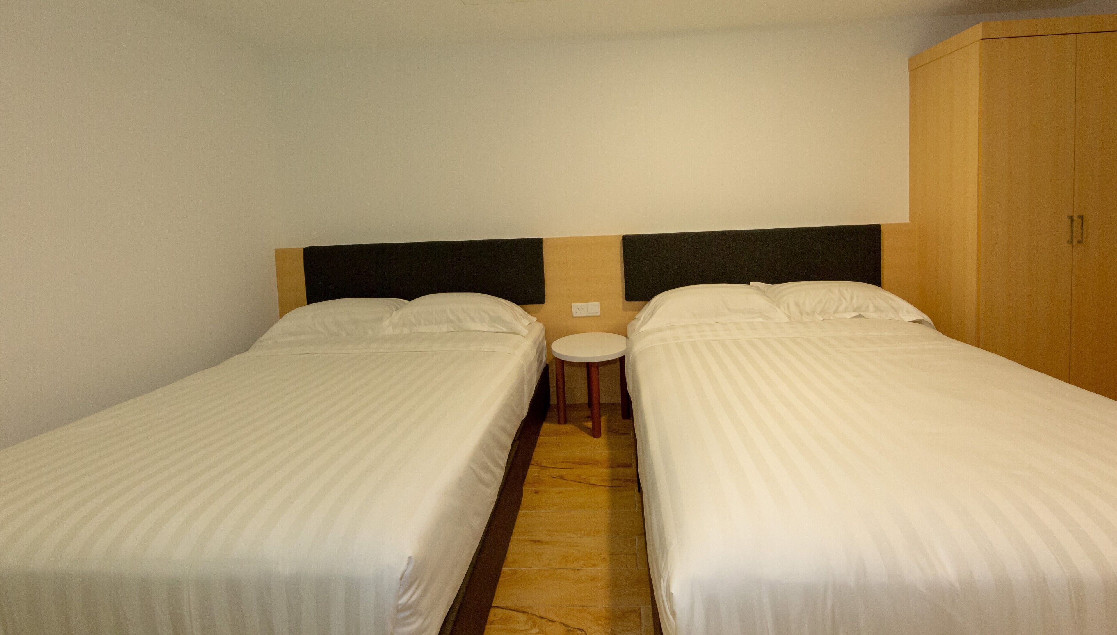 Quarto com duas camas de solteiro, uma mesa redonda pequena e um guarda-roupa.