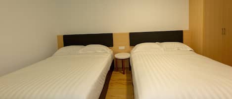 Quarto com duas camas de solteiro, uma mesa redonda pequena e um guarda-roupa.