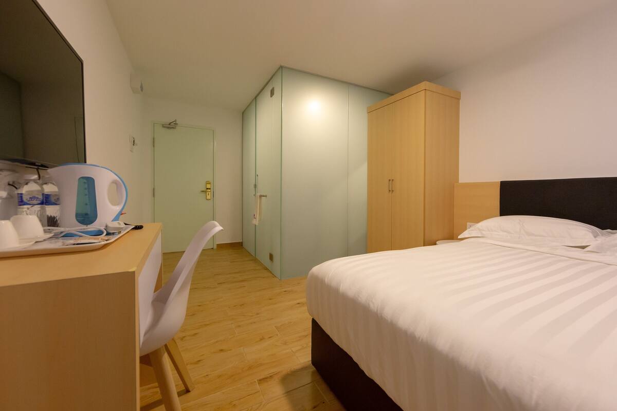 Une chambre d’hôtel comprenant un lit, un bureau avec une chaise, une armoire et une porte de salle de bain.