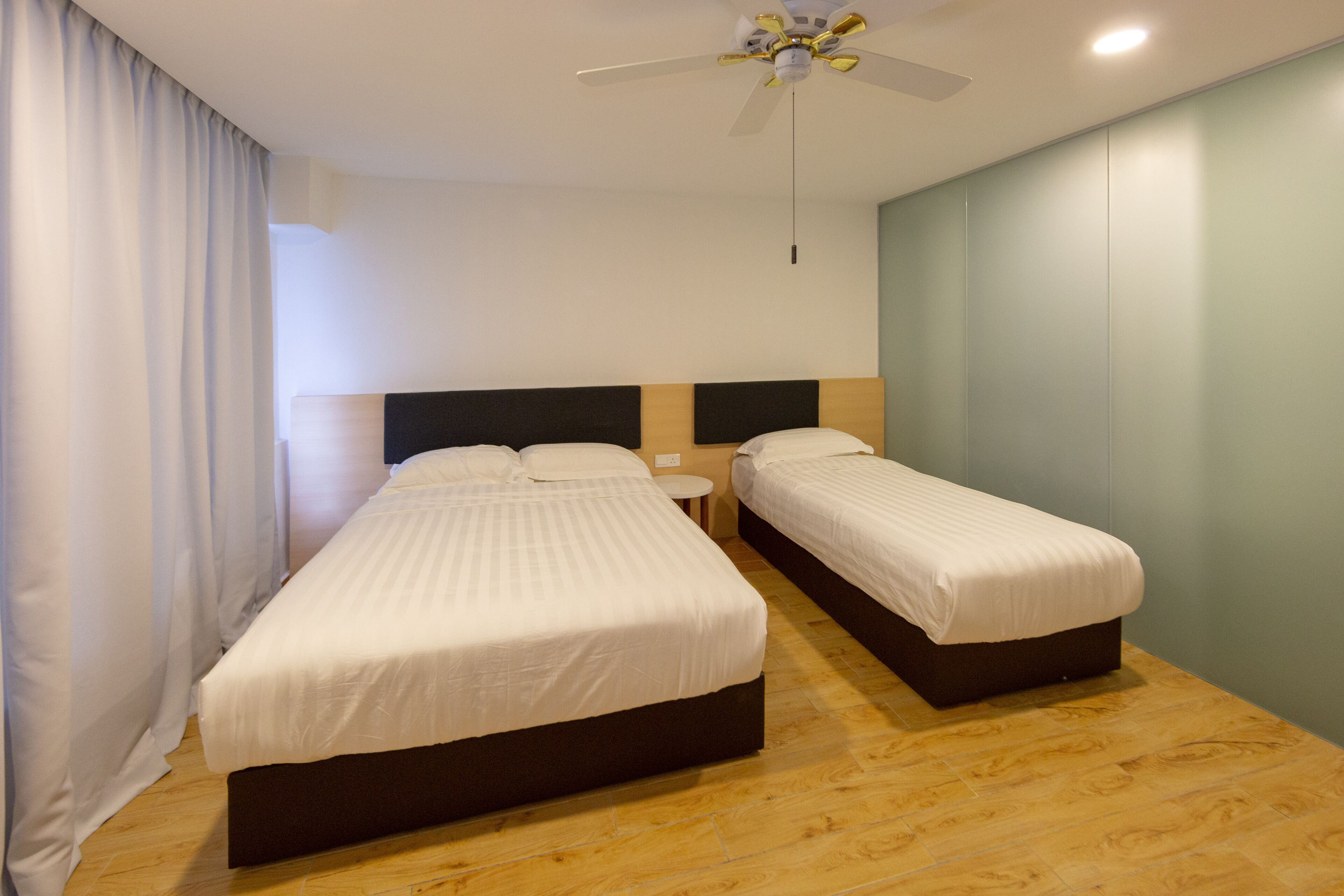 A double room with two beds, a ceiling fan, a round nightstand, and a light switch on the wall.