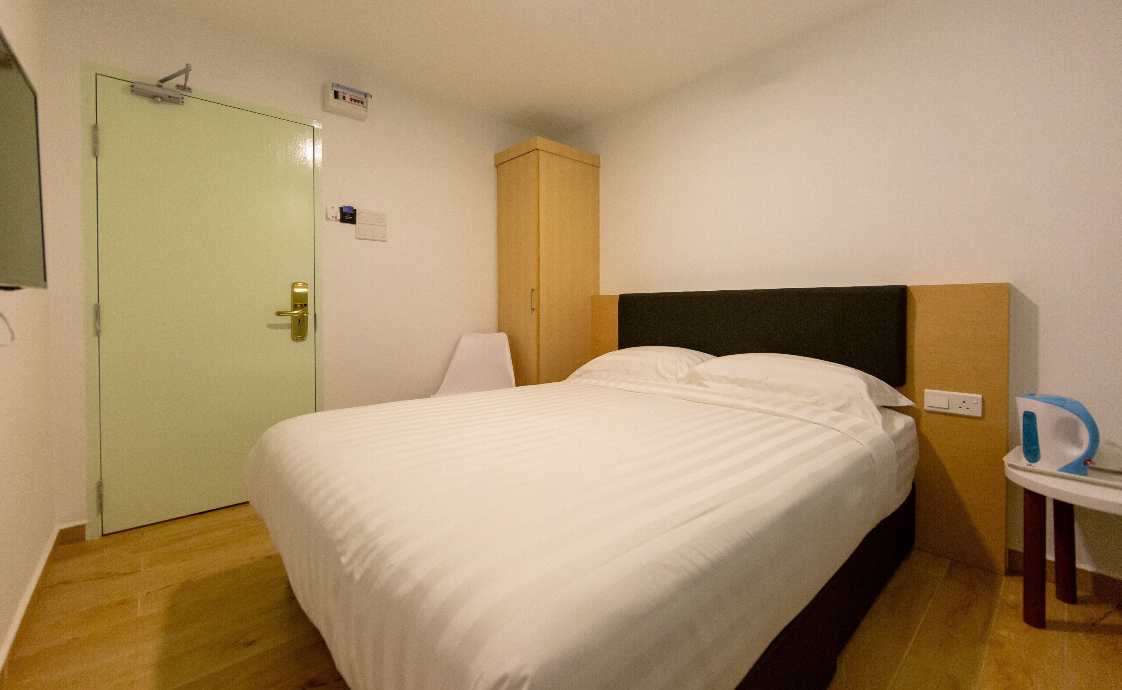 A single bed with a wooden headboard, a bedside table, and a green door.