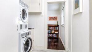 Een wasruimte met een wasmachine en droger, een boekenplank vol boeken, en een deur naar een andere kamer.