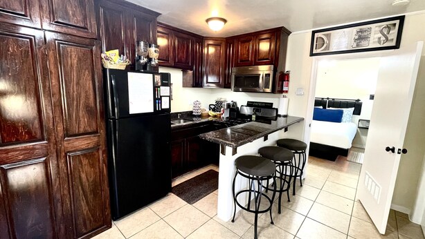 Cocina compacta con alacenas de madera oscura, refrigerador negro, microondas y una pequeña isla con taburetes de bar.