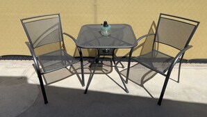 Una mesa metálica y dos sillas con respaldo de malla, situadas frente a una pared amarilla.