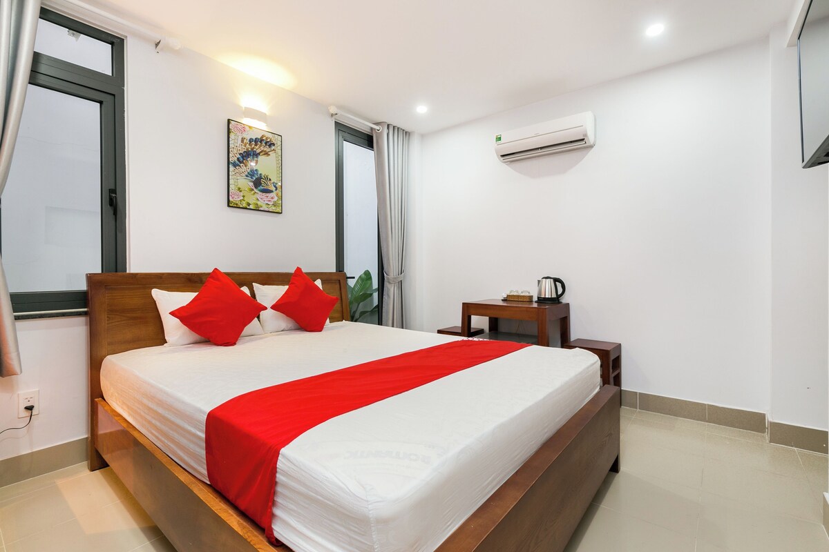 Een hotelkamer met een bed, nachtkastje, airconditioning en een raam met gordijnen.