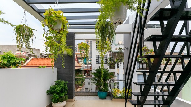 Un balcón moderno al aire libre con plantas en macetas, una escalera de metal y vistas de edificios vecinos.