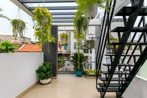 A modern outdoor balcony with potted plants, a metal staircase, and a view of neighboring buildings. - Super OYO 520 Friendly Homestay (Ho Chi Minh City)