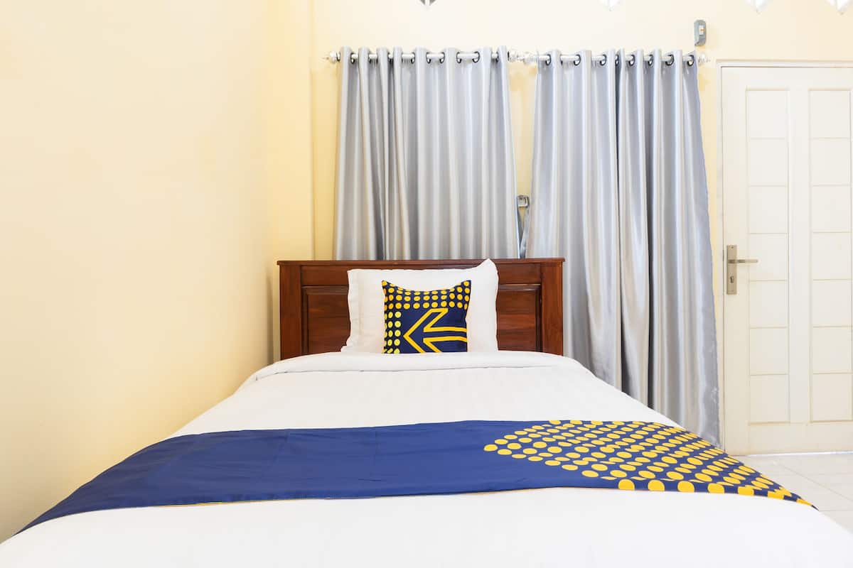 A neatly made bed with a blue and yellow patterned bedspread, a white pillow with a geometric design, and a wooden headboard.