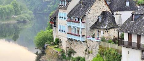 Un edificio junto al río con muros de piedra y varios balcones, reflejado en aguas tranquilas.