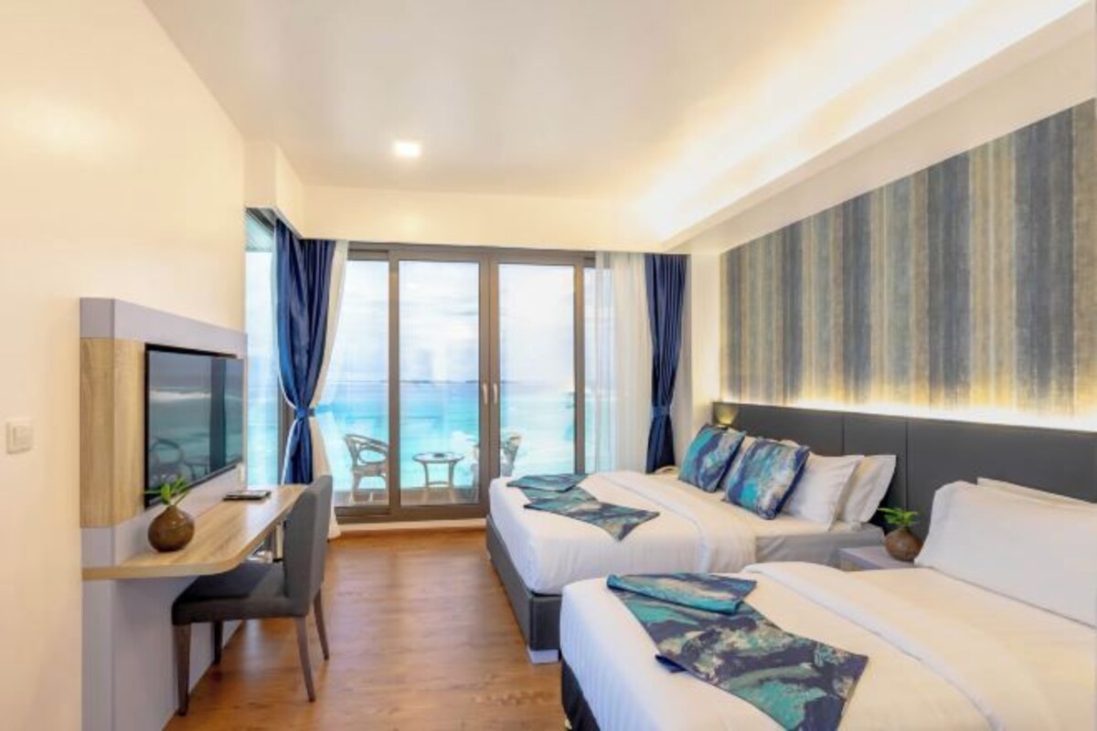 Ein Hotelzimmer mit zwei Betten, einem Schreibtisch, einem Fernseher und Meerblick durch große Fenster.