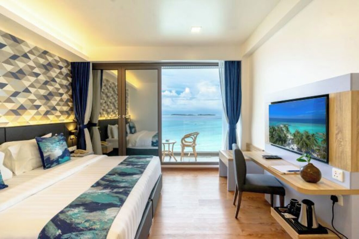 Ein Hotelzimmer mit Bett, Schreibtisch, Fernseher und Blick aufs Meer.
