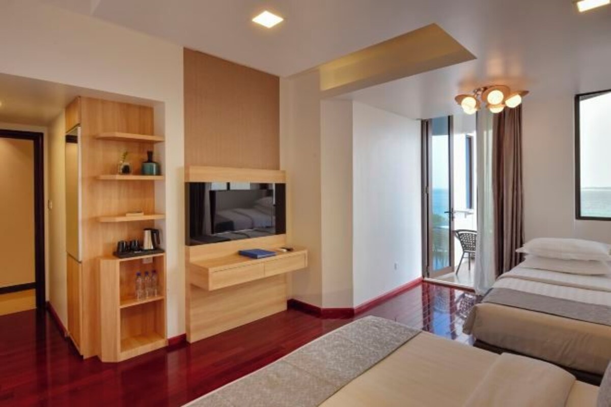 A hotel room with a wooden entertainment unit, a flat-screen TV, a bed with two pillows, and a view of the outdoors.