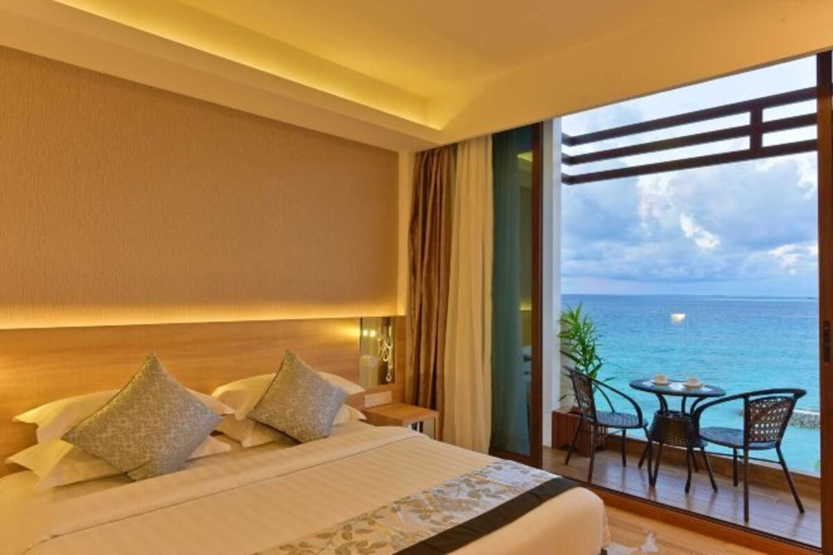 Ein Hotelzimmer mit einem großen Bett, einem Balkon mit Meerblick und einem kleinen Tisch mit Stühlen.