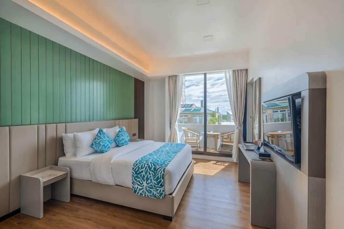A modern hotel room with a bed, a TV, a desk, and a balcony with a view.