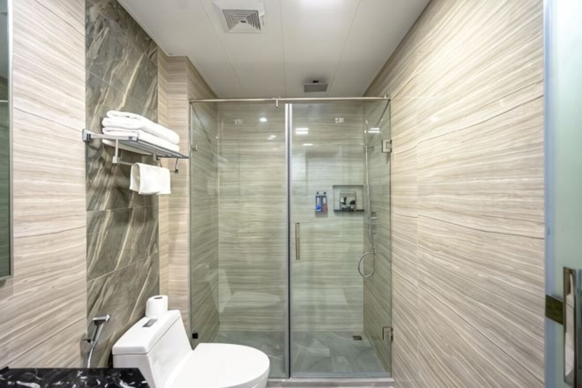 Ein modernes Badezimmer mit einer gläsernen Duschkabine, Marmorwänden, einer Toilette und einem Handtuchhalter.