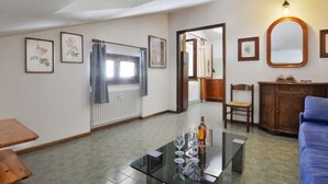Una sala de estar con una mesa de centro de vidrio, un sofá azul, un aparador de madera y cuadros enmarcados en las paredes.