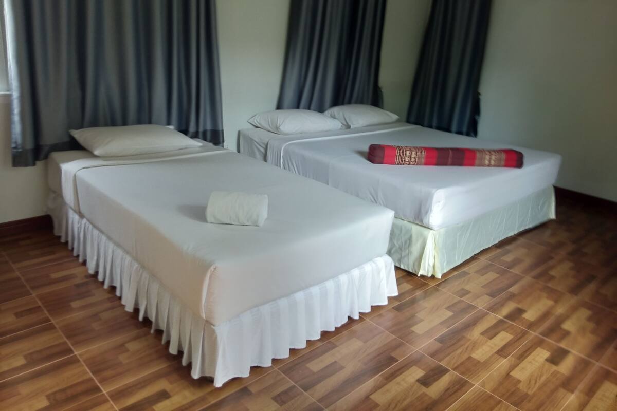 A hotel room with two single beds, a wooden floor, and a window with curtains.
