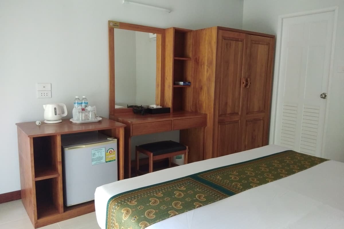 A hotel room with a bed, a wooden desk with a mirror, a small refrigerator, and a wardrobe.