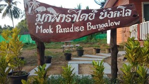 Señal para Mook Paradise Bungalow con temática tropical, rodeada de plantas en macetas y un camino.