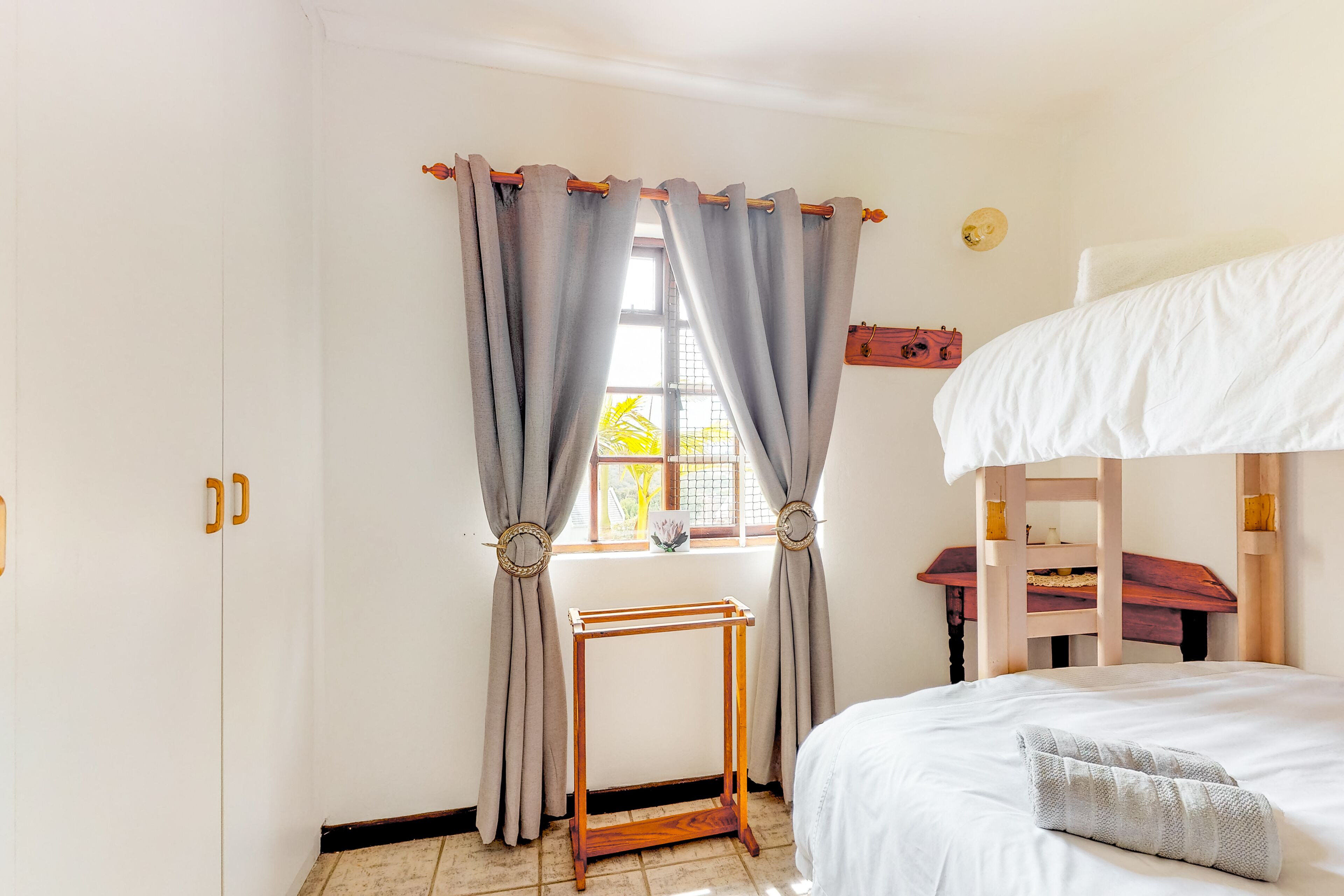A bedroom with a bunk bed, a wooden desk, and a window with curtains.