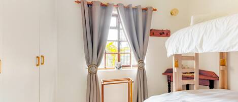 A bedroom with a bunk bed, a wooden desk, and a window with curtains.