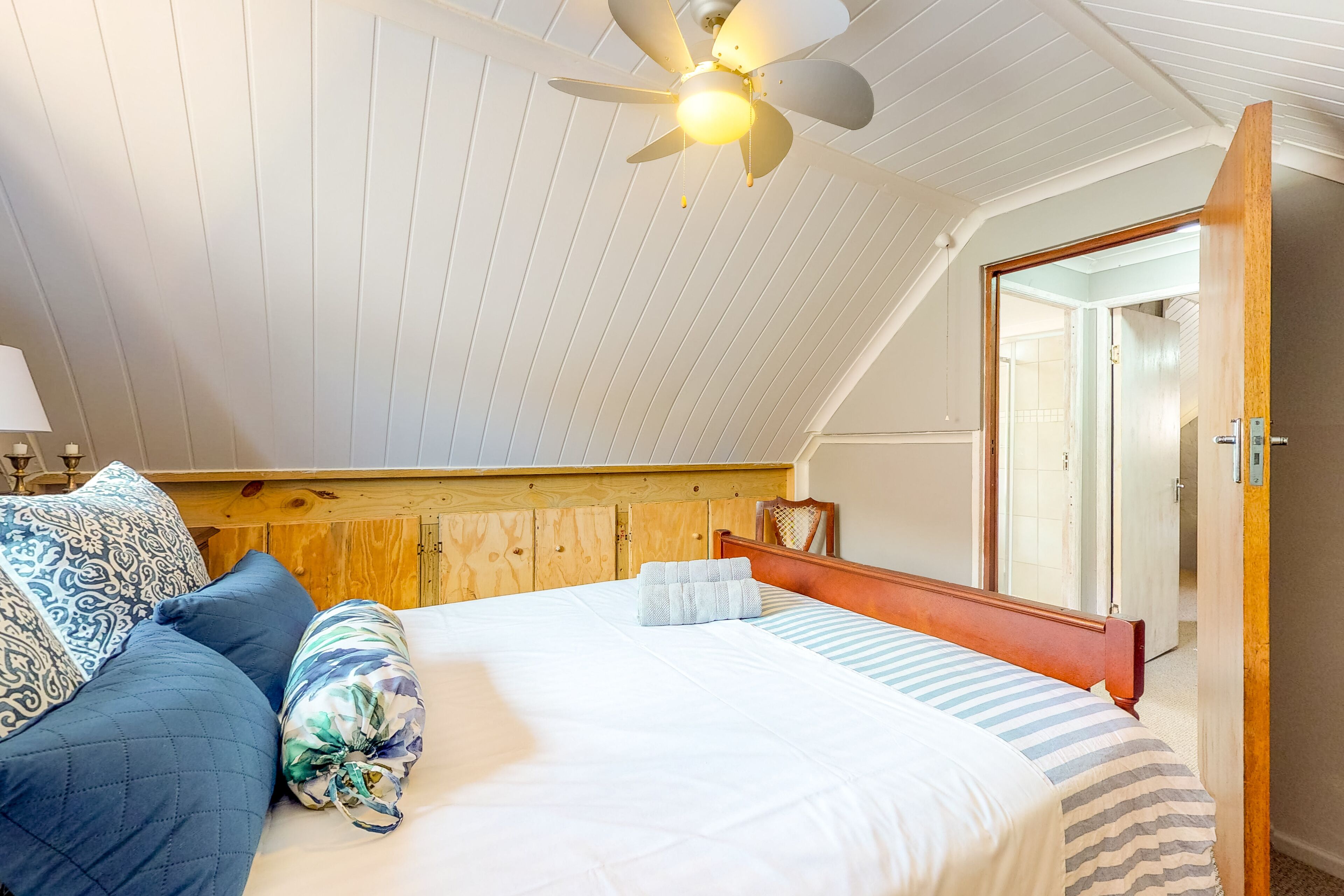 A bedroom with a sloped ceiling, a bed with a striped bedspread, and a ceiling fan.