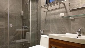 Un baño con ducha de vidrio, inodoro blanco y lavabo con mueble de madera.