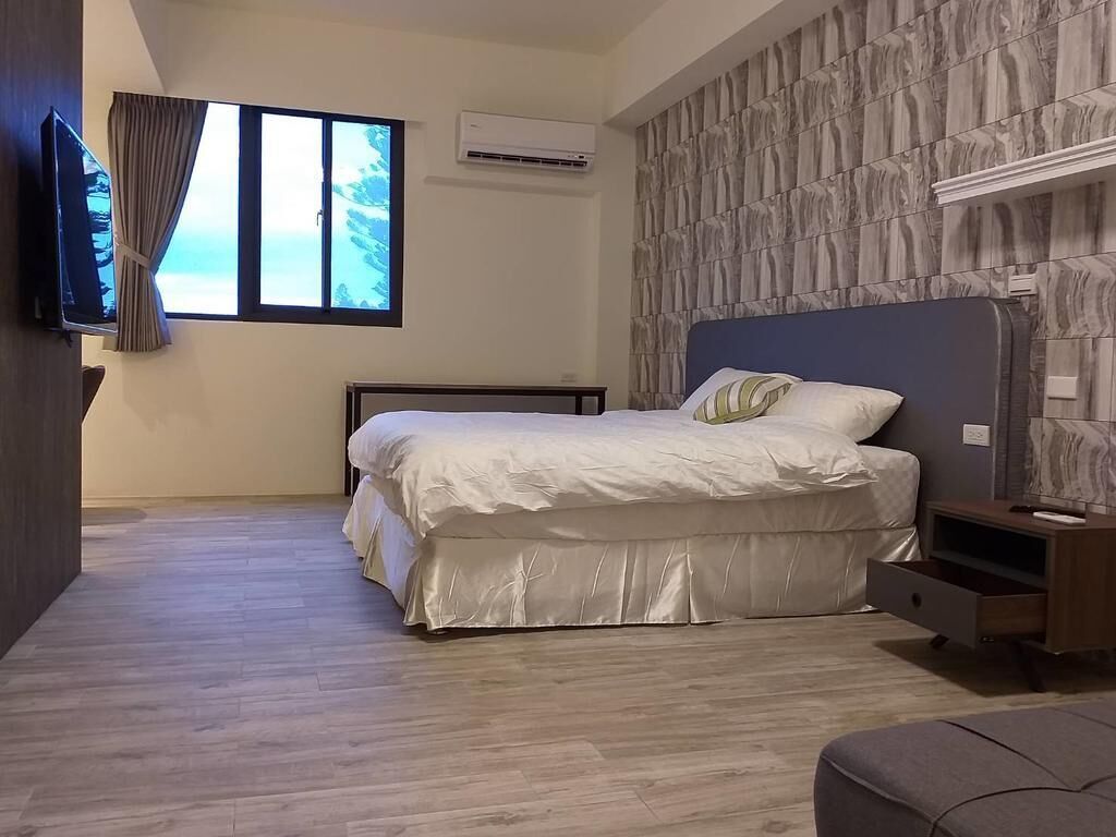 A bedroom with a bed, a TV, an air conditioner, and a view of the sea.