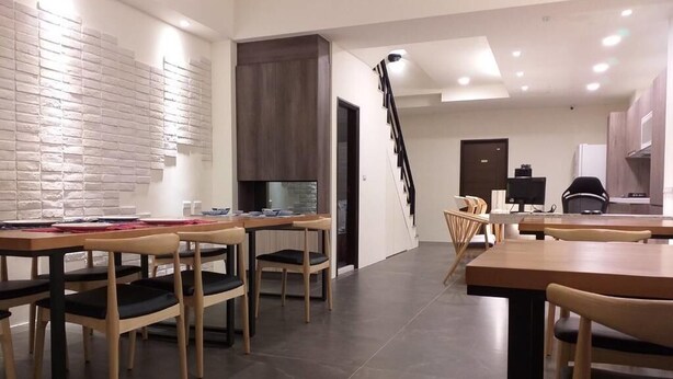 Un comedor moderno con mesas y sillas de madera, una pared de acento de ladrillo y una escalera que conduce a otro nivel.