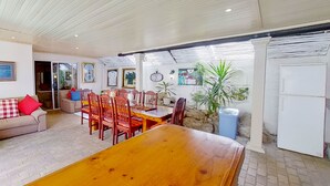A spacious living area with a wooden dining table, red and blue chairs, a beige sofa with red cushions, and a white refrigerator. - Executive Couples Suite Strand (Cape Town)