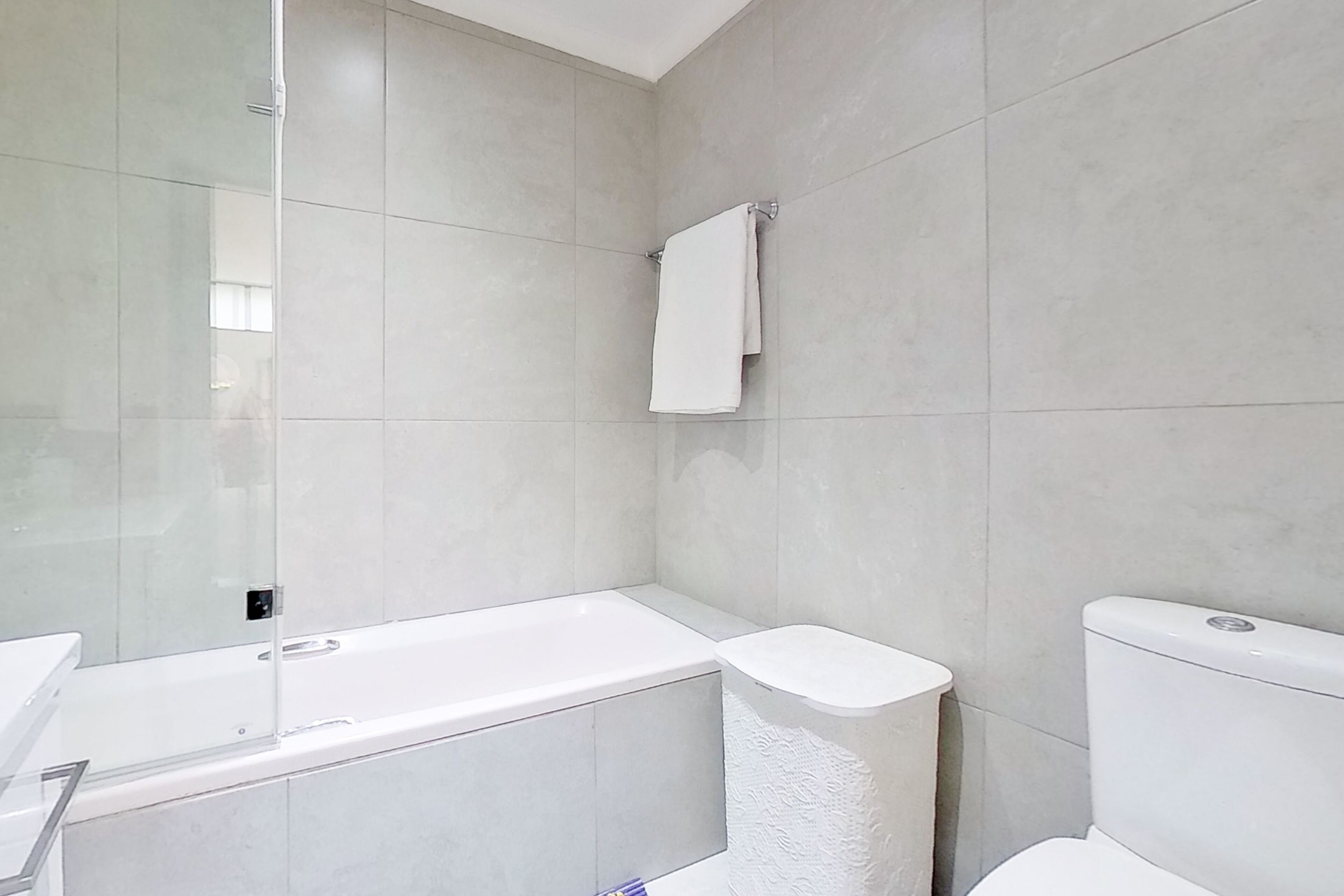 A modern bathroom with a bathtub, toilet, and glass shower enclosure.