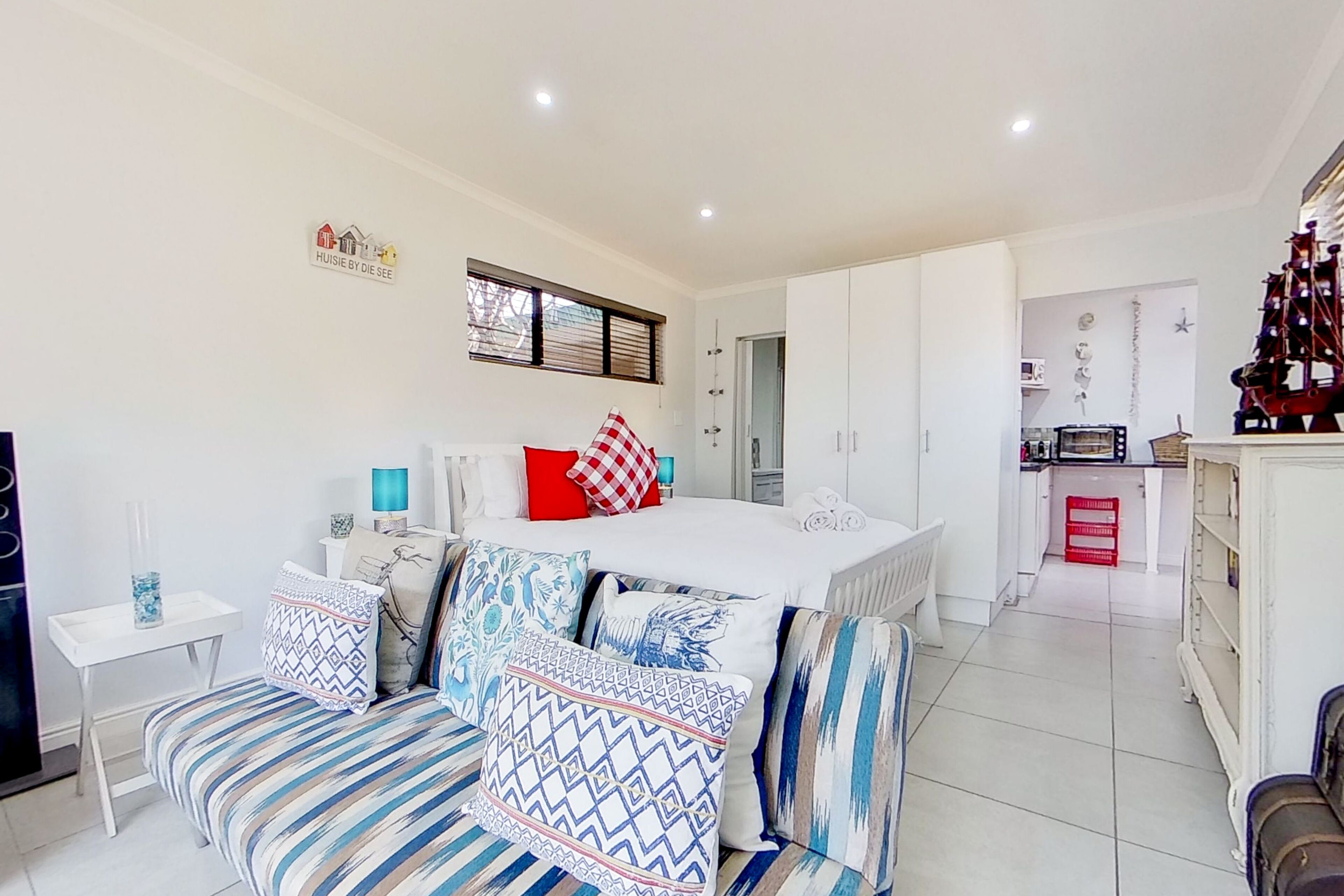 A modern bedroom with a large bed, a sofa, and a kitchenette in the background.