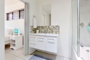 A bathroom with a white vanity, a glass shower enclosure, and a window with blinds.
