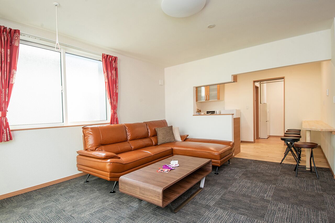 A modern living room with a brown leather sofa, a wooden coffee table, and a small table with chairs.