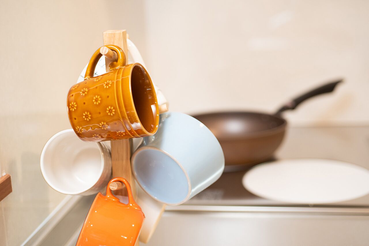Une cuisine avec un plan de travail blanc, une poêle brune et une pile de tasses colorées.