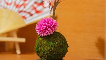 Eine Mooskugelvase mit rosa Blüten und einem Fächer im Hintergrund.